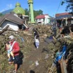 Warga berjalan di atas tumpukan material akibat banjir bandang di Jorong Galuang, Nagari Sungai Pua, Agam, Sumatera Barat, Senin (13/05). ANTARA FOTO/Iggoy el Fitra